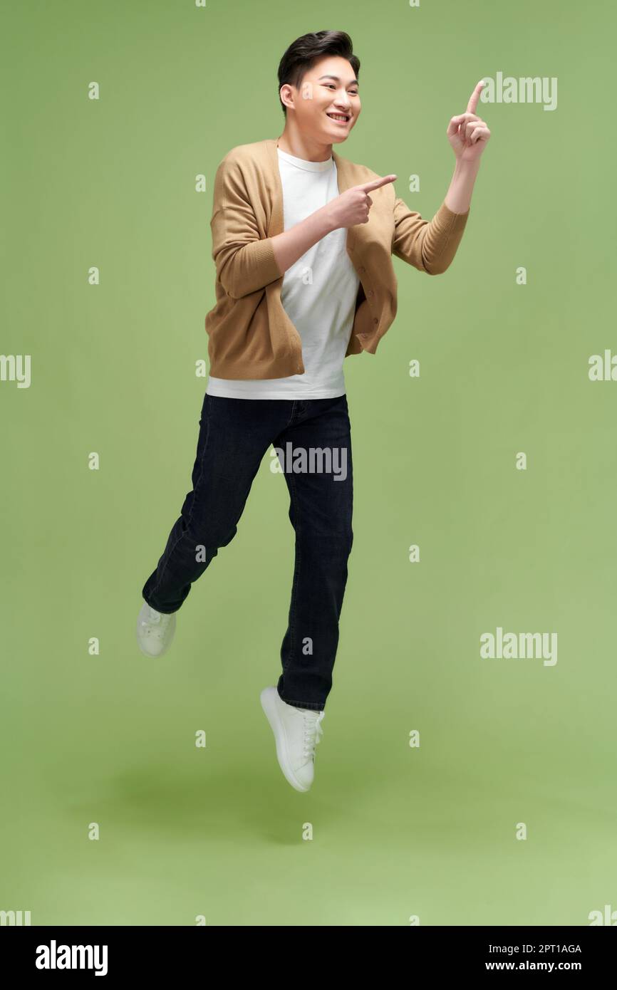 Excited handsome asian guy jumping in the air, pointing at copy space