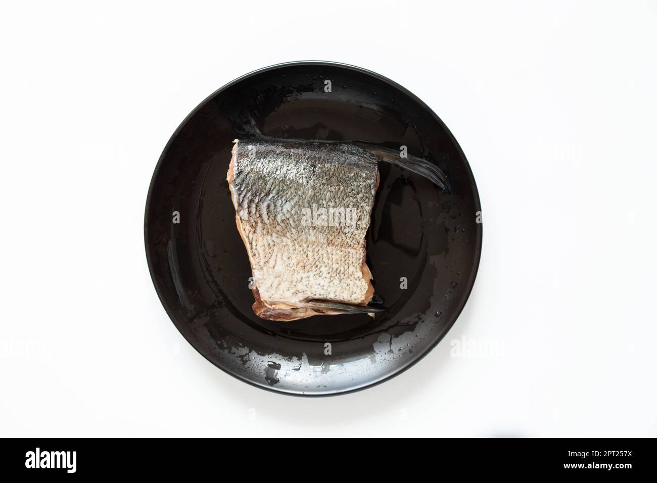 A raw piece of silver carp lies on a black plate on a white background Stock Photo