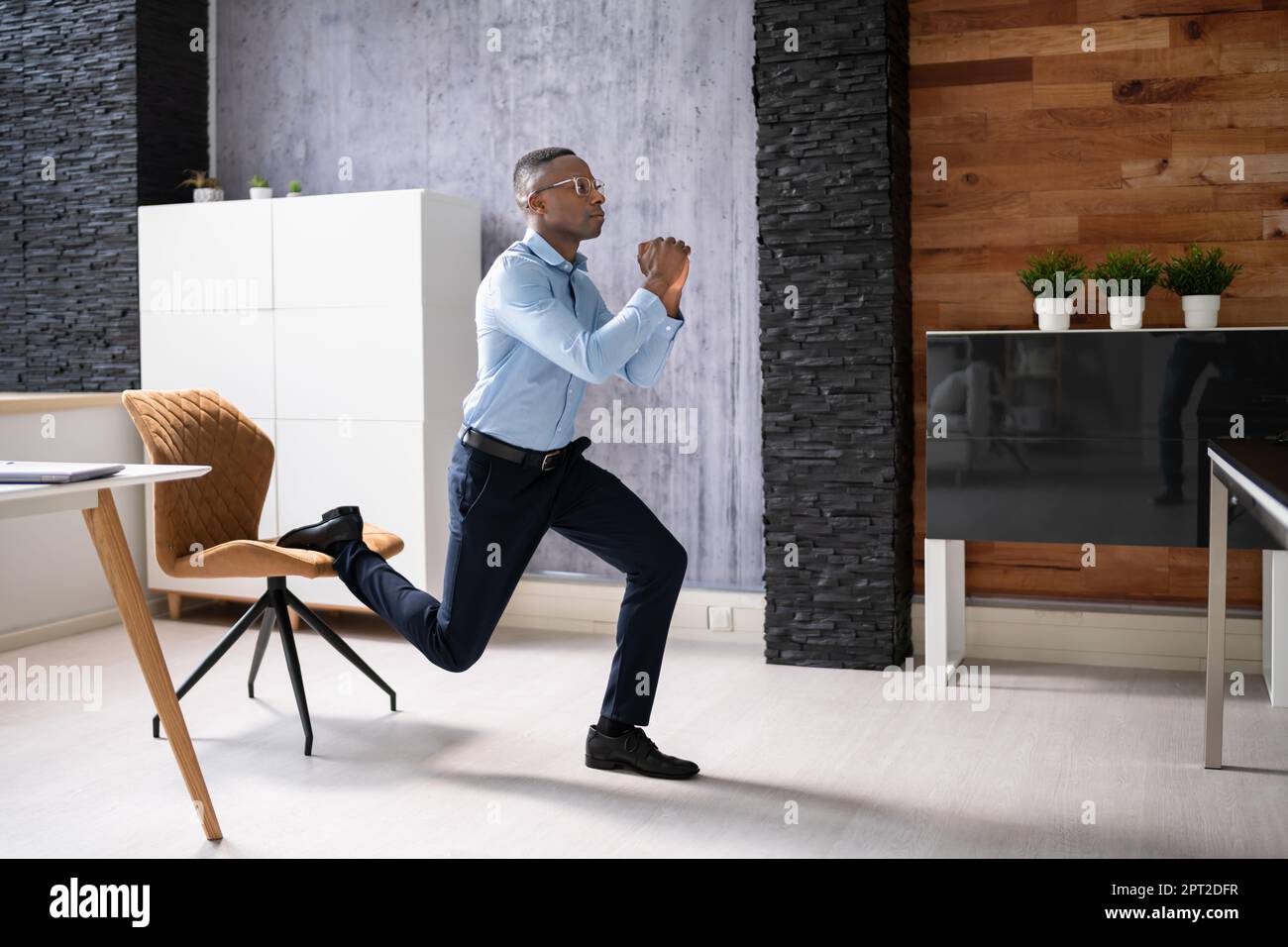 African Employee Doing Bulgarian Split Squat Exercise In Office Stock Photo