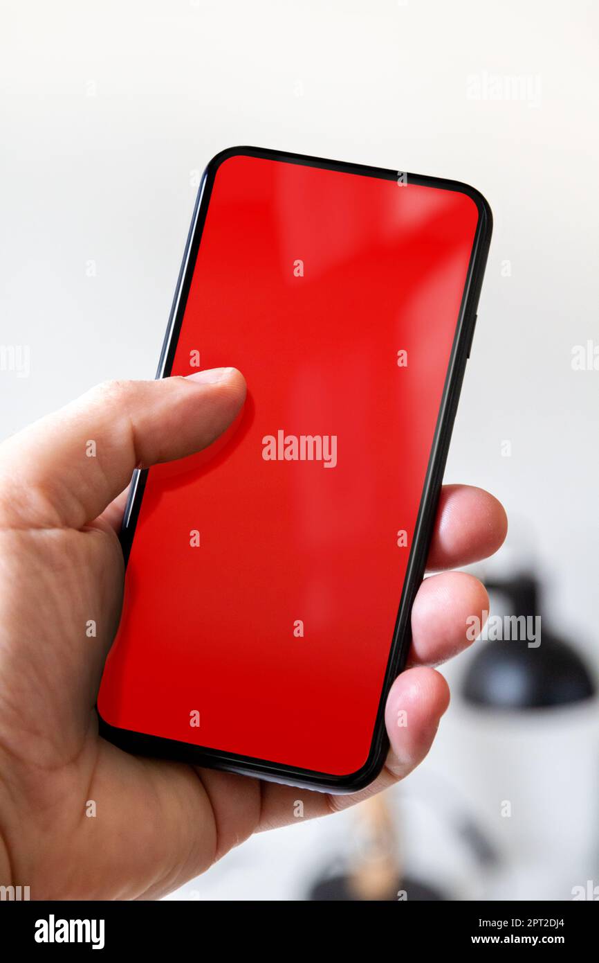 Hand holding a smartphone with blank red screen. White office