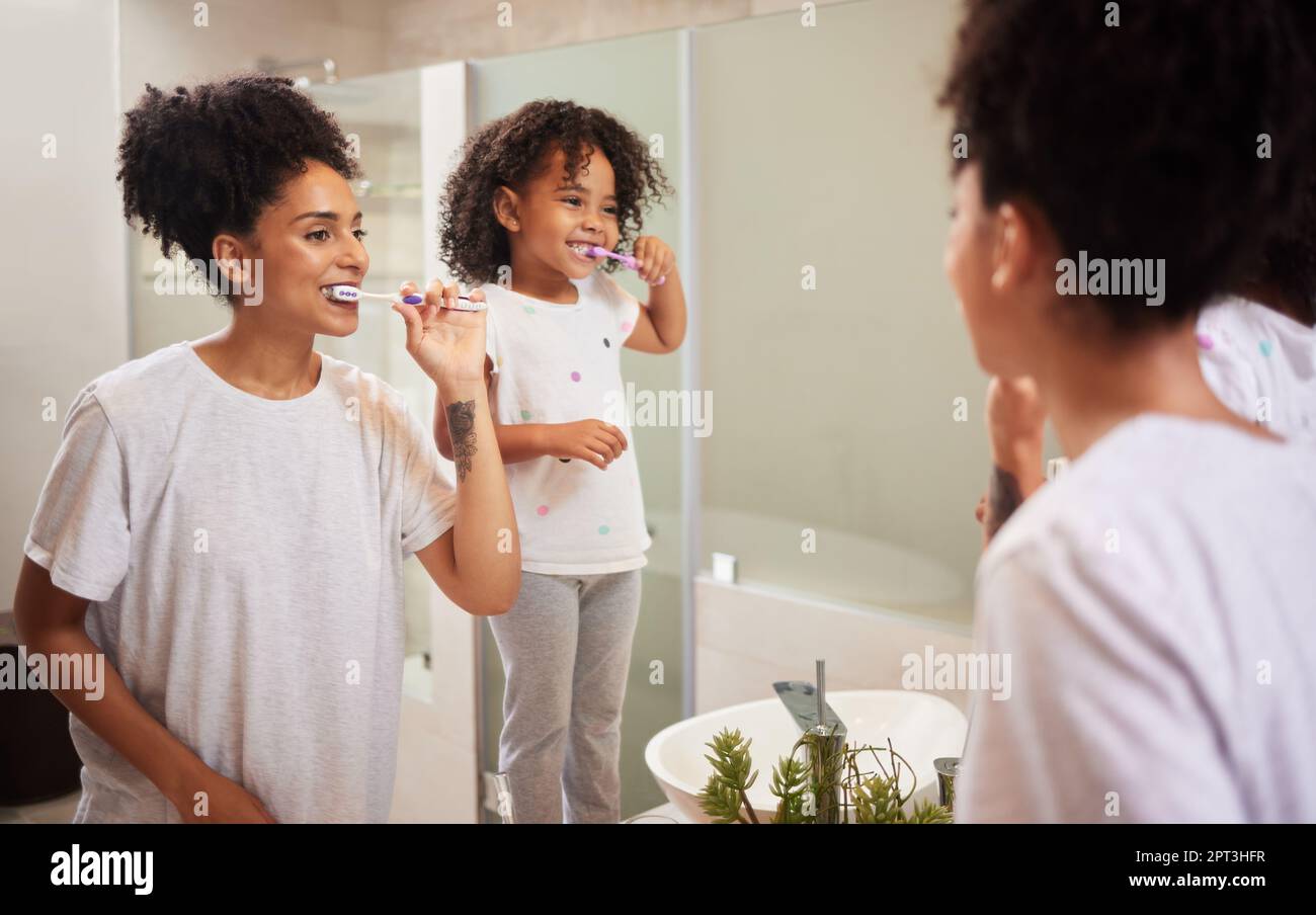 Mirror reflection of mom and girl brushing teeth together while bonding