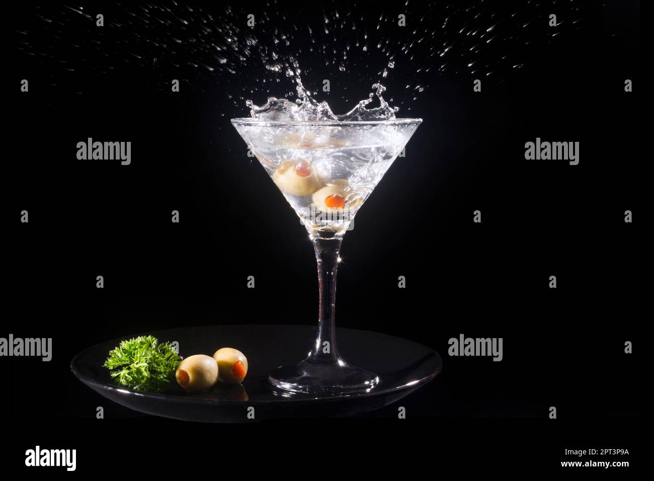 Splashing martini cocktail drink with green olives is on black