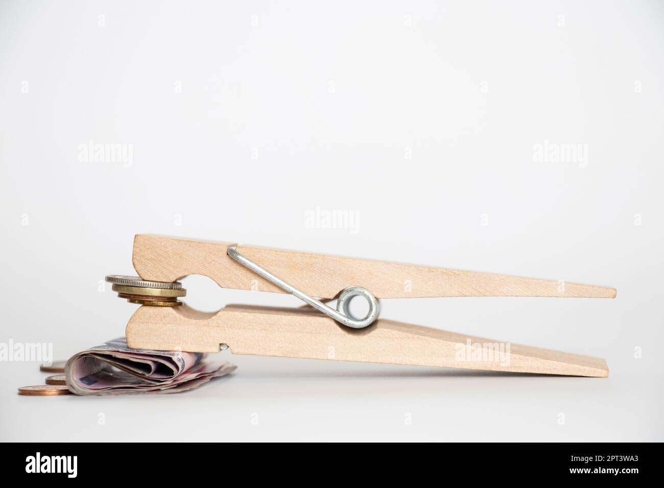 A wooden big clothespin holds Ukrainian coins and paper hryvnias on a