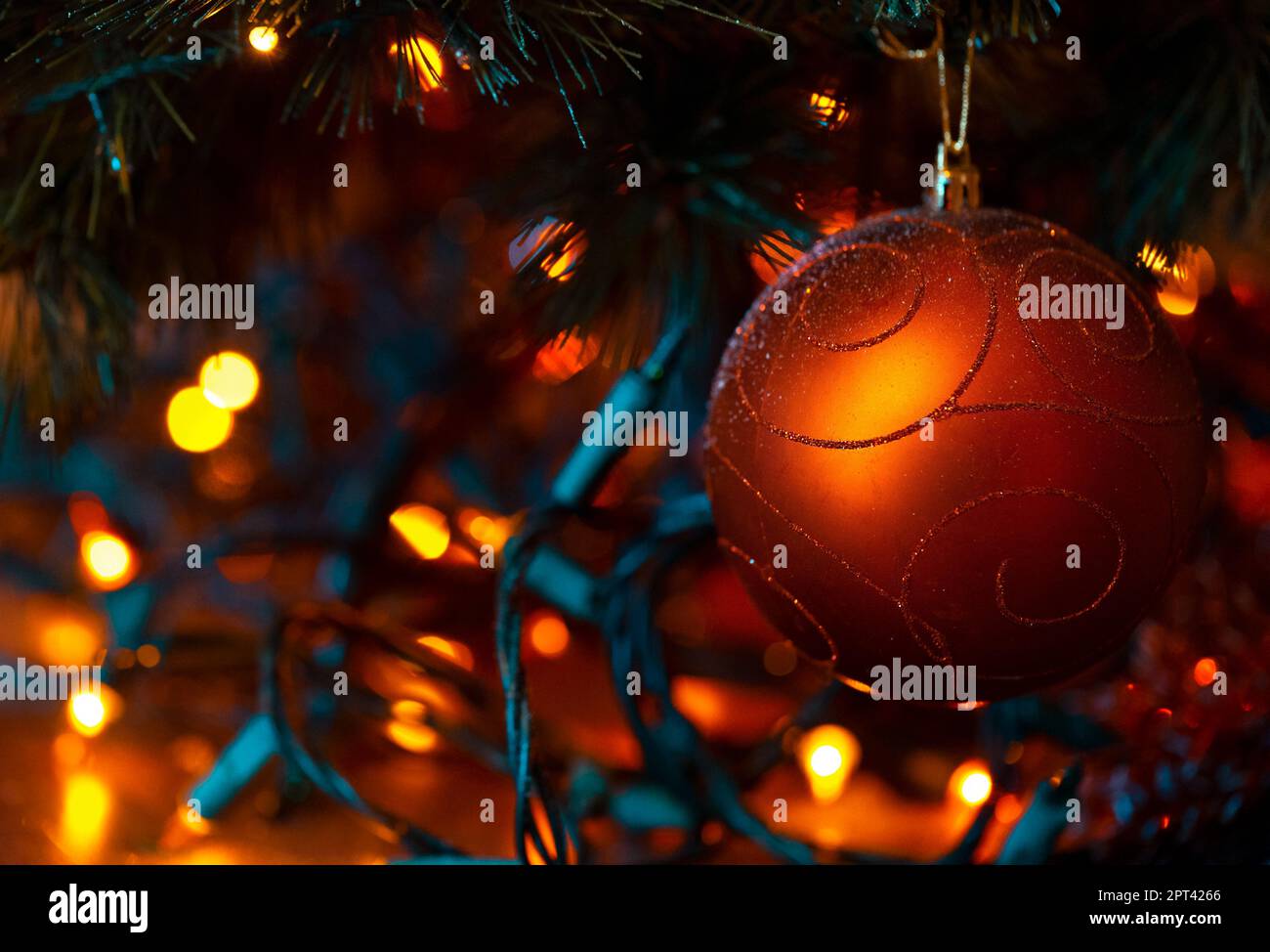 Beautiful Red Christmas Ball. Xmas Tree Decorated with Festive Glowing Garland and Bronze Red Shiny Ball. Decorative Baubles for X-Mas and New Year Ho Stock Photo