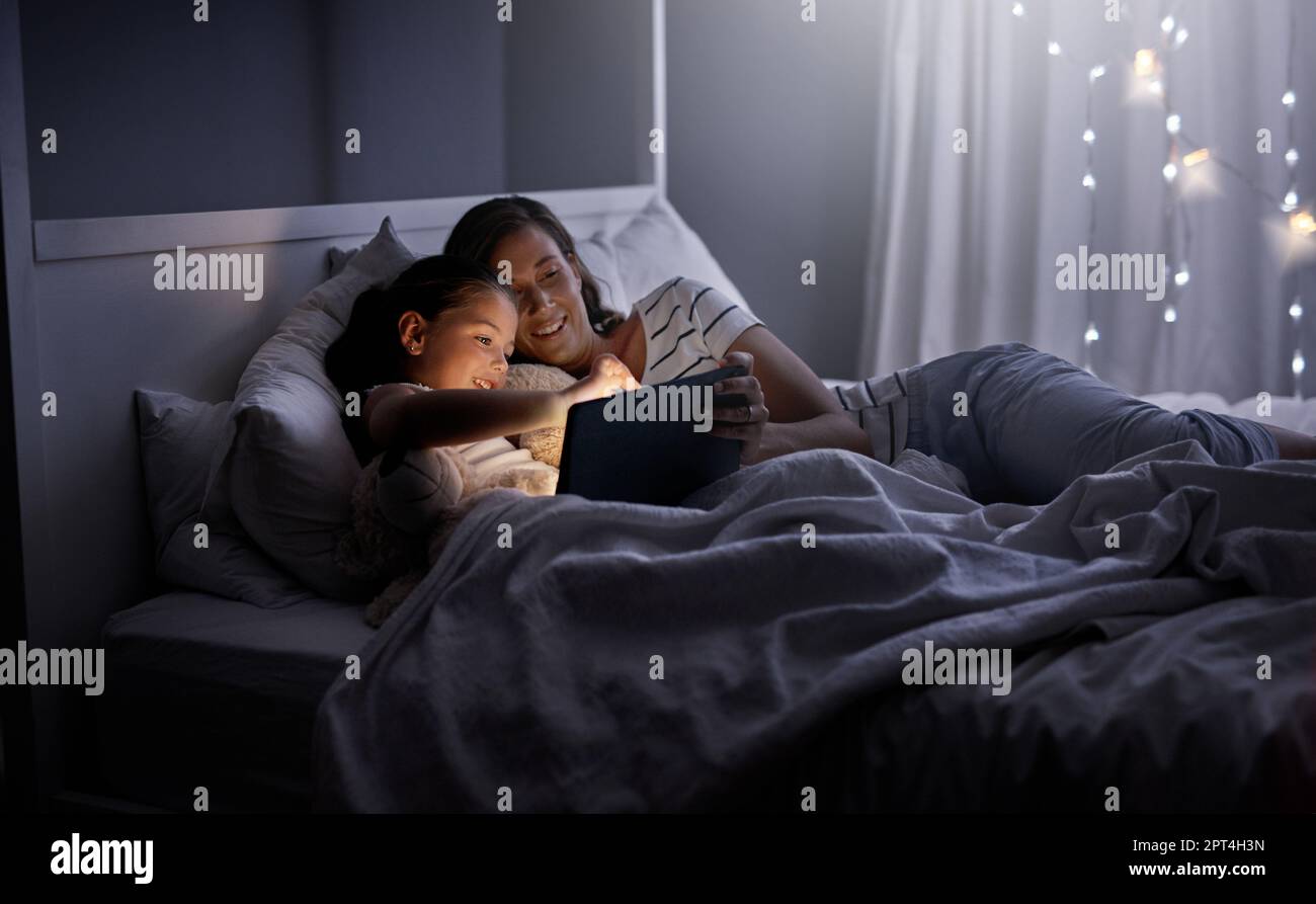 Snuggling up with a good story on their device. a mother and her little daughter using a digital tablet together in bed at night Stock Photo