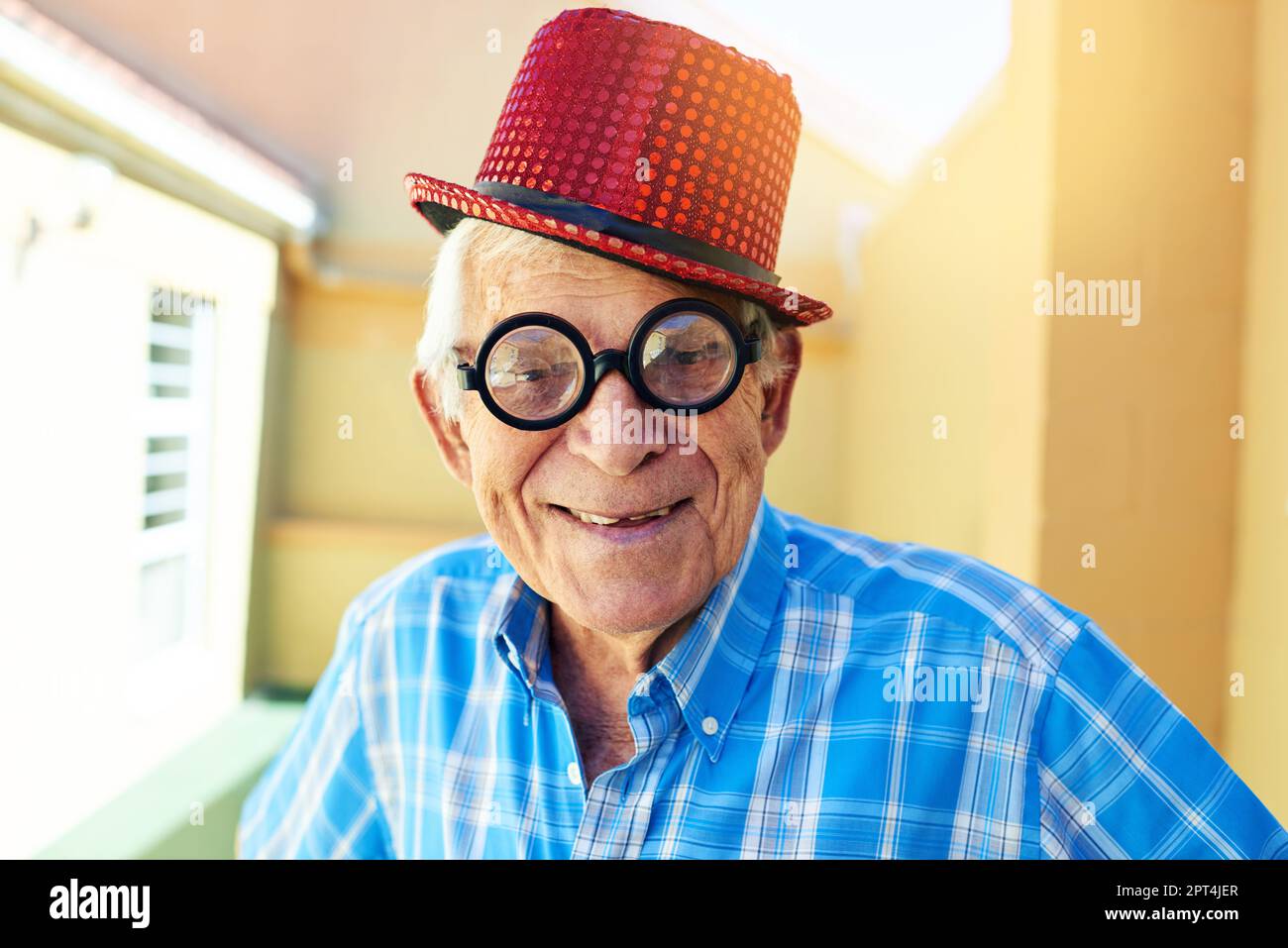 I can actually see through these glasses. a carefree elderly man wearing funky glasses and a hat while posing for the camera inside a building Stock Photo