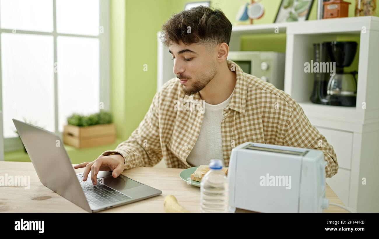 Young arab man having breakfast using laptop at home Stock Photo