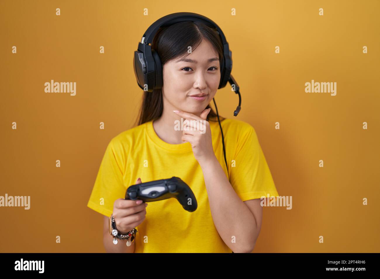 Chinese young woman playing video game holding controller looking confident at  the camera smiling with crossed arms and hand raised on chin. thinking  Stock Photo - Alamy