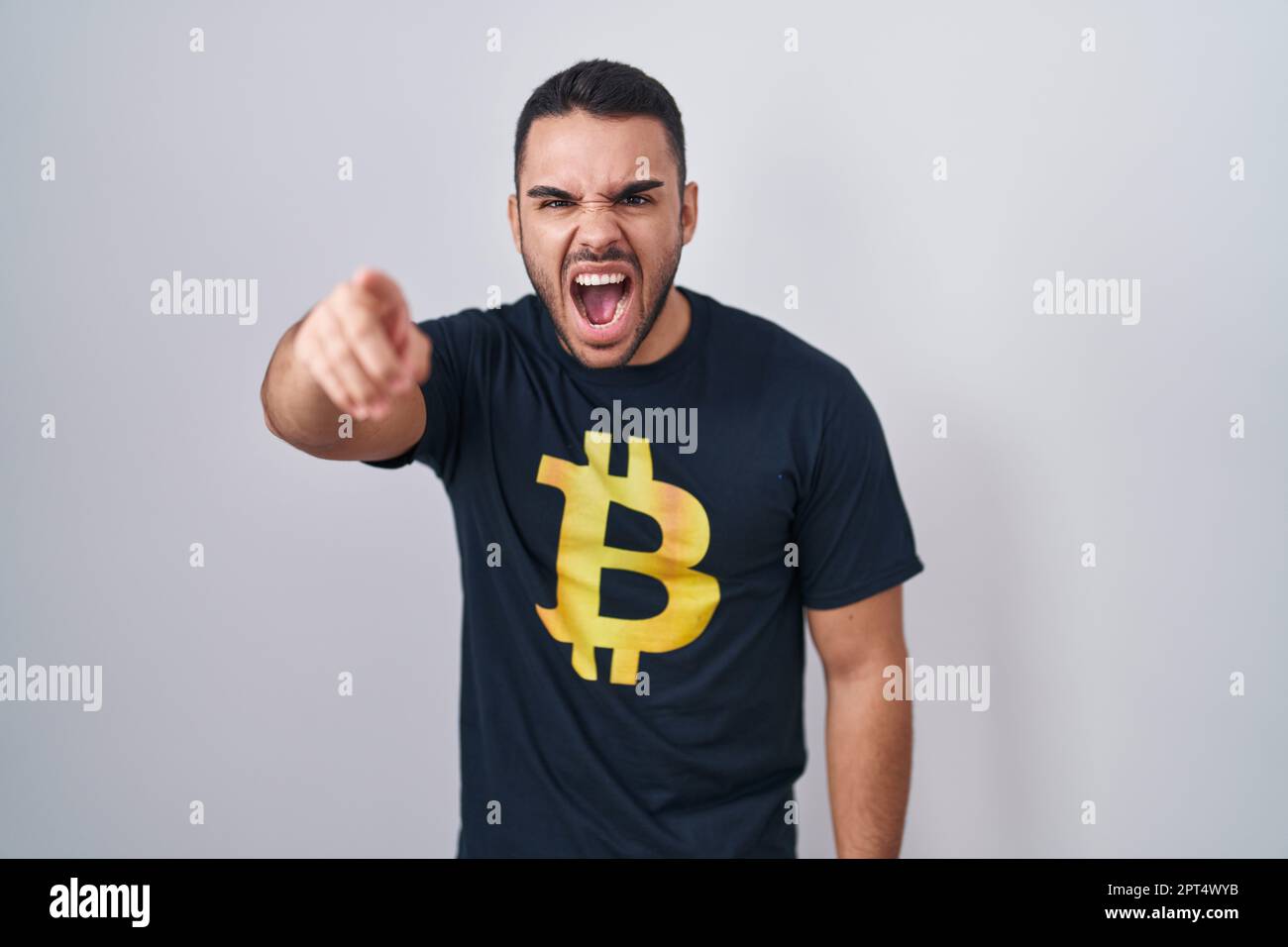 Young hispanic man wearing bitcoin t shirt pointing displeased and ...