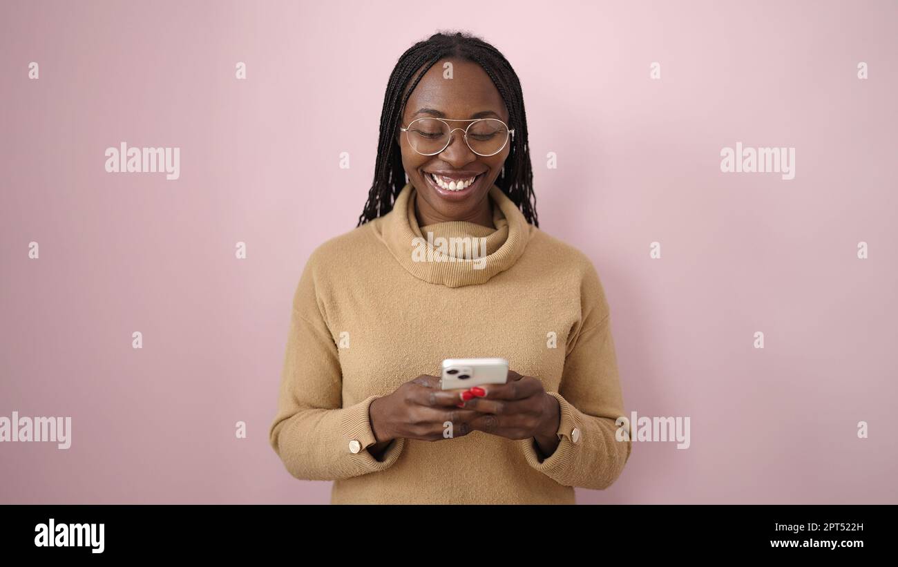 African woman smiling using smartphone over isolated pink background ...