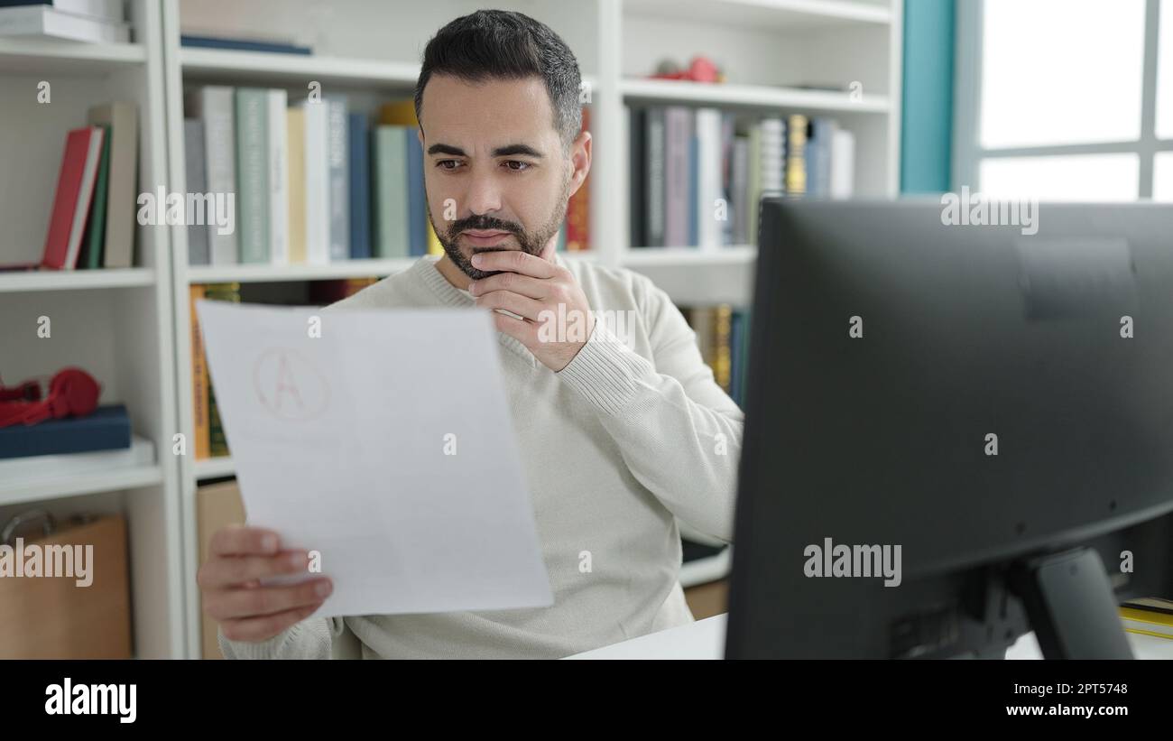 Young hispanic man student using computer reading document at library ...