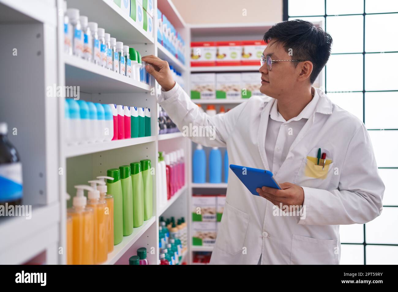 Young chinese man pharmacist using touchpad working at pharmacy Stock ...