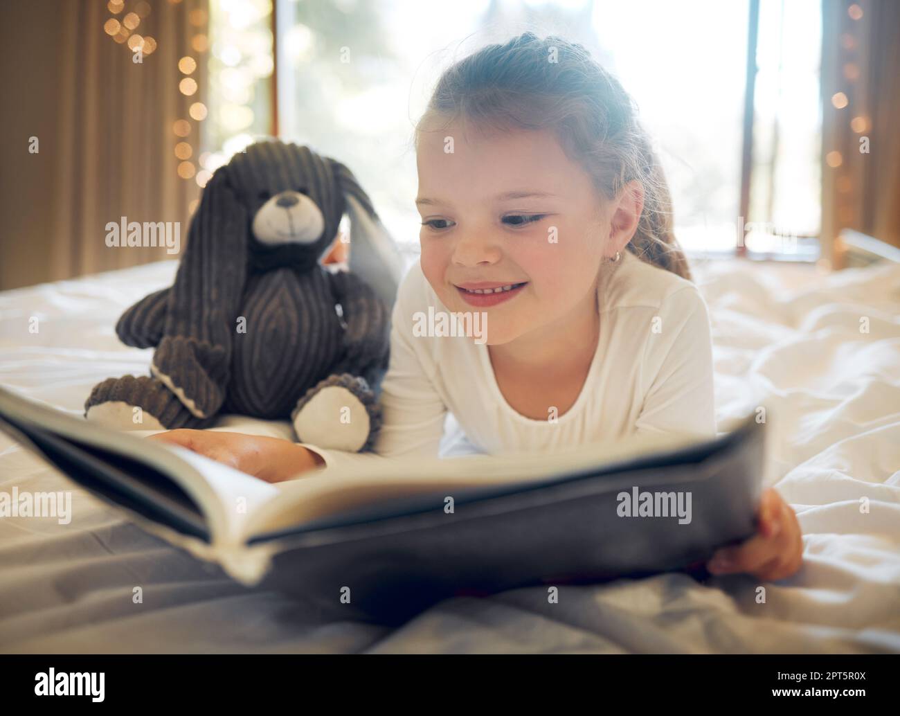 Happy smiling little girl lying on a bed at home and reading a