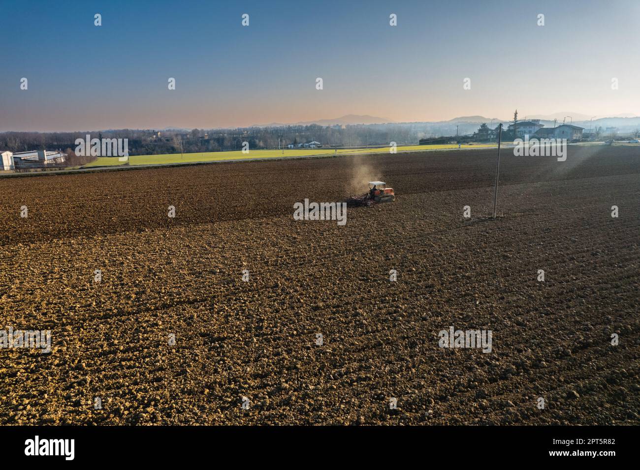 farmer driving a crawler tractor drags a cloud of dust behind