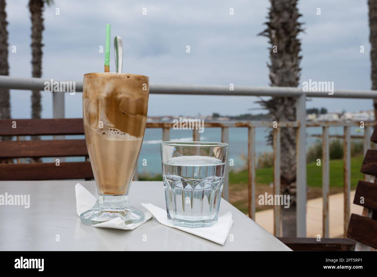 Coffee milkshake and a glass of water on a table at the beach, Paphos