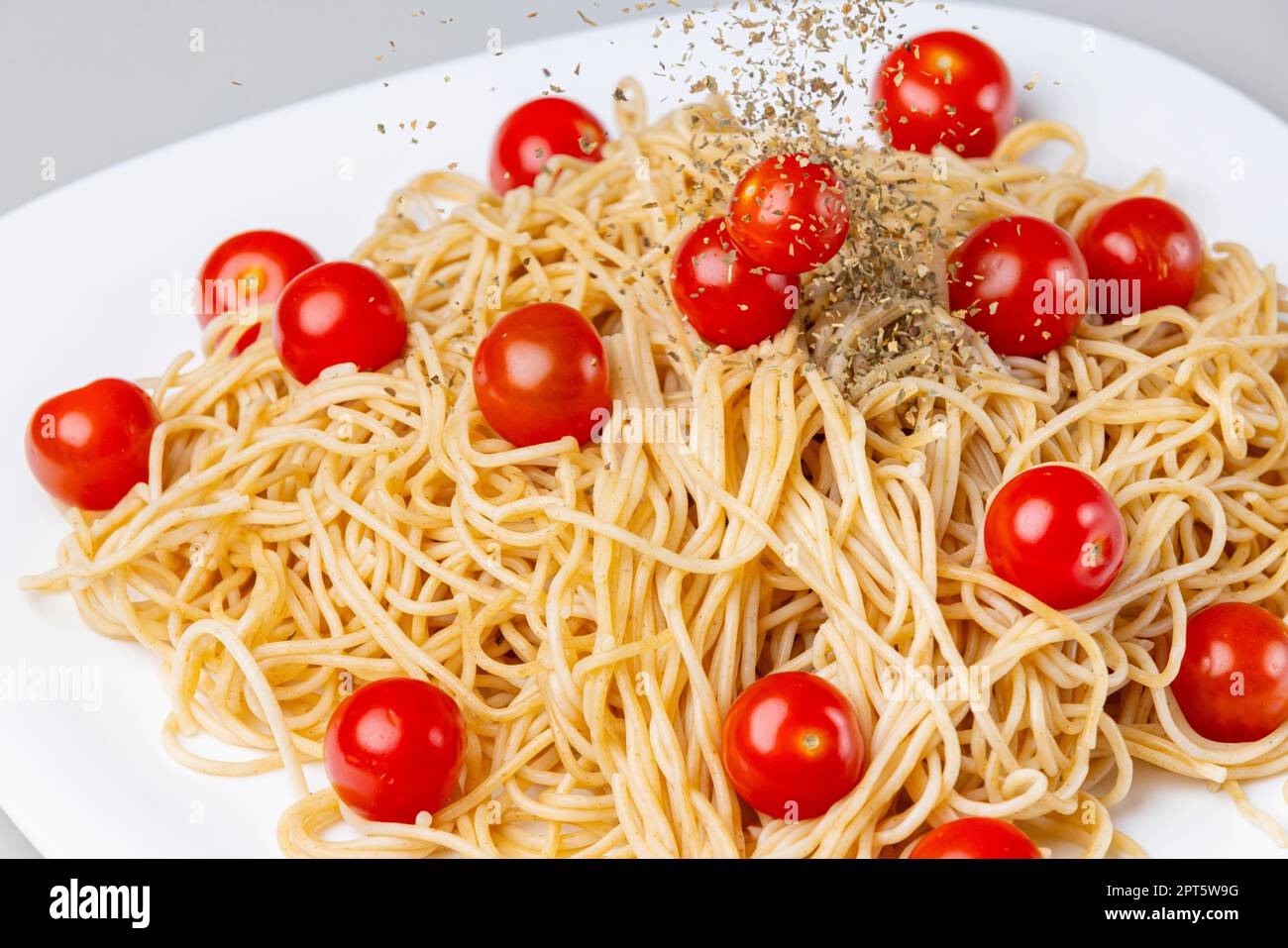 Dried basil is sprinkled over spaghetti with cocktail tomatoes, food photography, white plate, white background Stock Photo