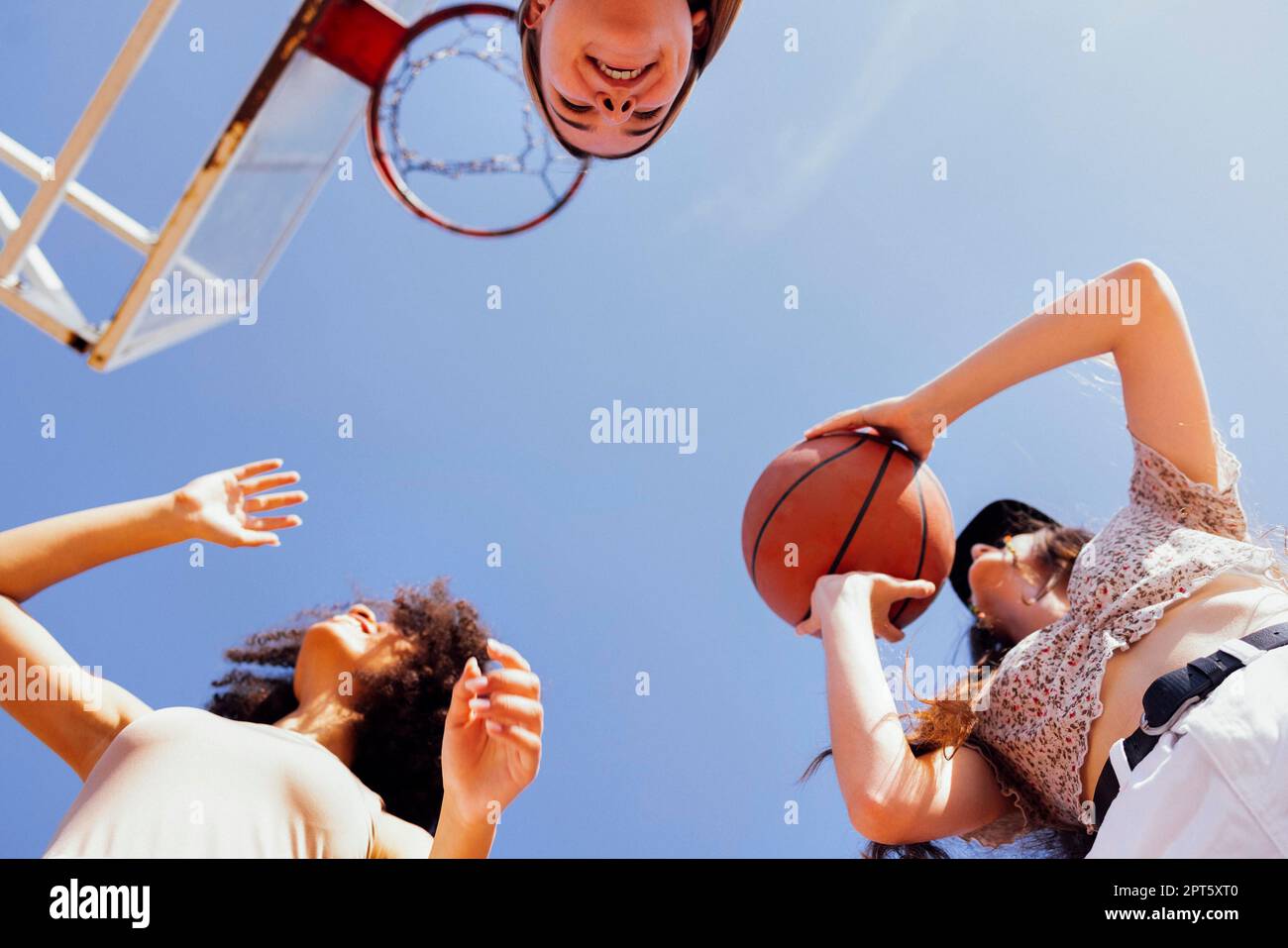 Multicultural group of young female friends bonding outdoors and having fun. Stylish cool teen girls gathering at basketball court, friends playing Stock Photo