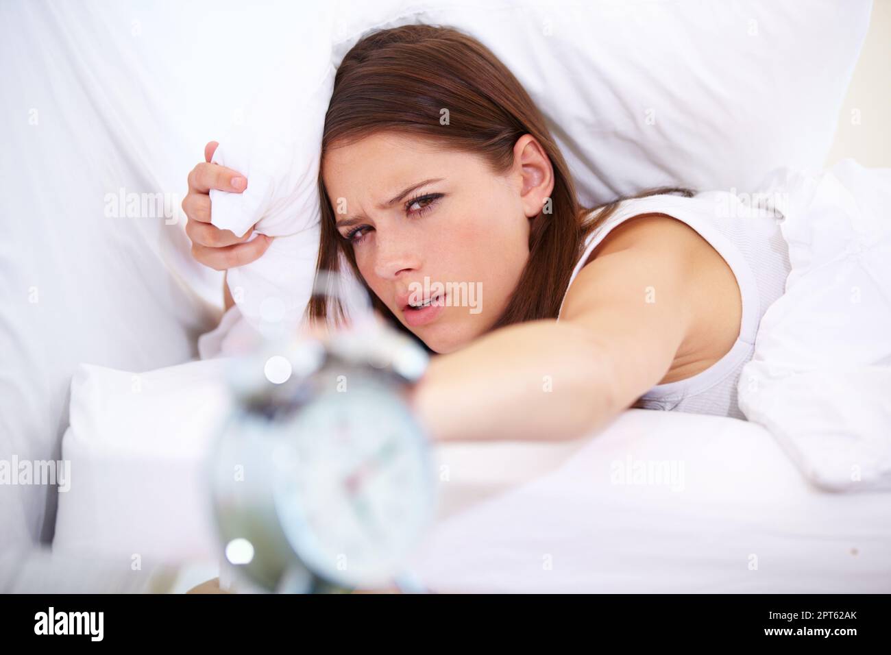 Why now. A young woman pressing the snooze button on her alarm clock