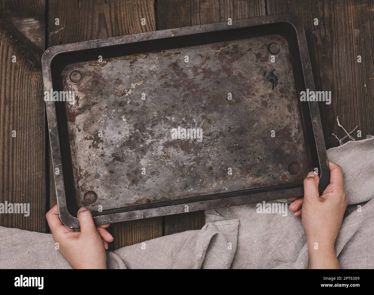 Two female hands hold a rectangular empty baking sheet on a brown wooden table, top view Stock Photo