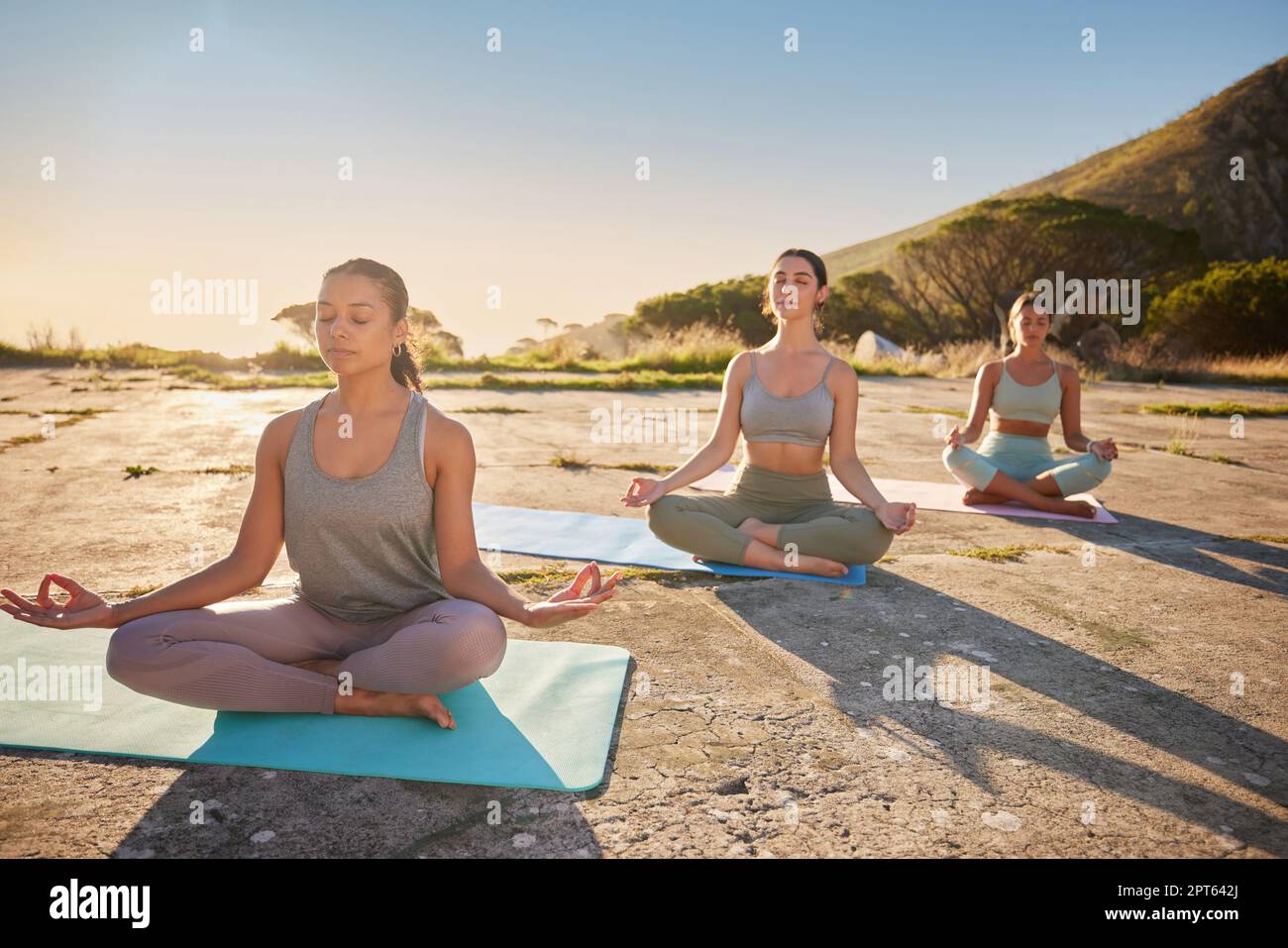 Full length yoga women meditating with legs crossed for outdoor practice in remote nature. Diverse group of mindful active friends bonding and balanci Stock Photo