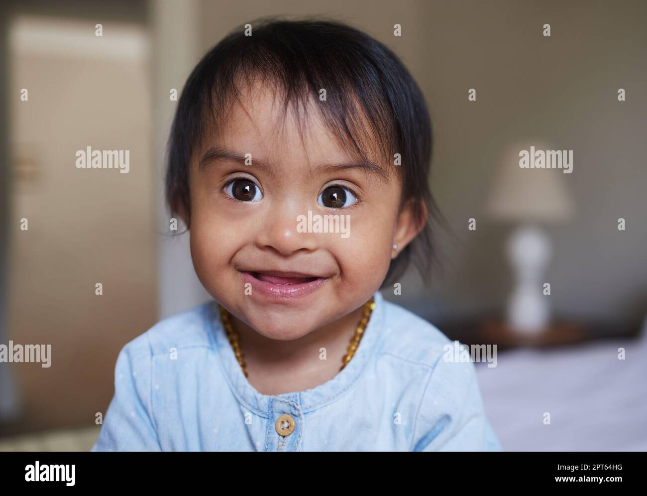 Happy, portrait smile and Down syndrome baby relaxing on a bed in happiness at home. Cheerful little child with genetic disorder or disability smiling Stock Photo