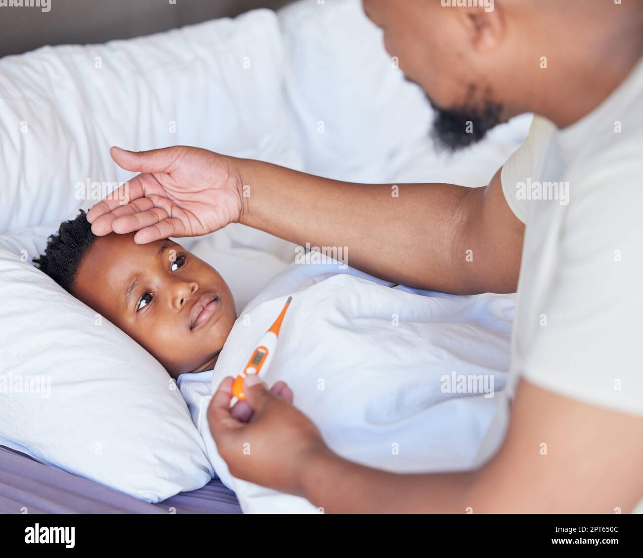 Sick little boy in bed while his father uses a thermometer to check his