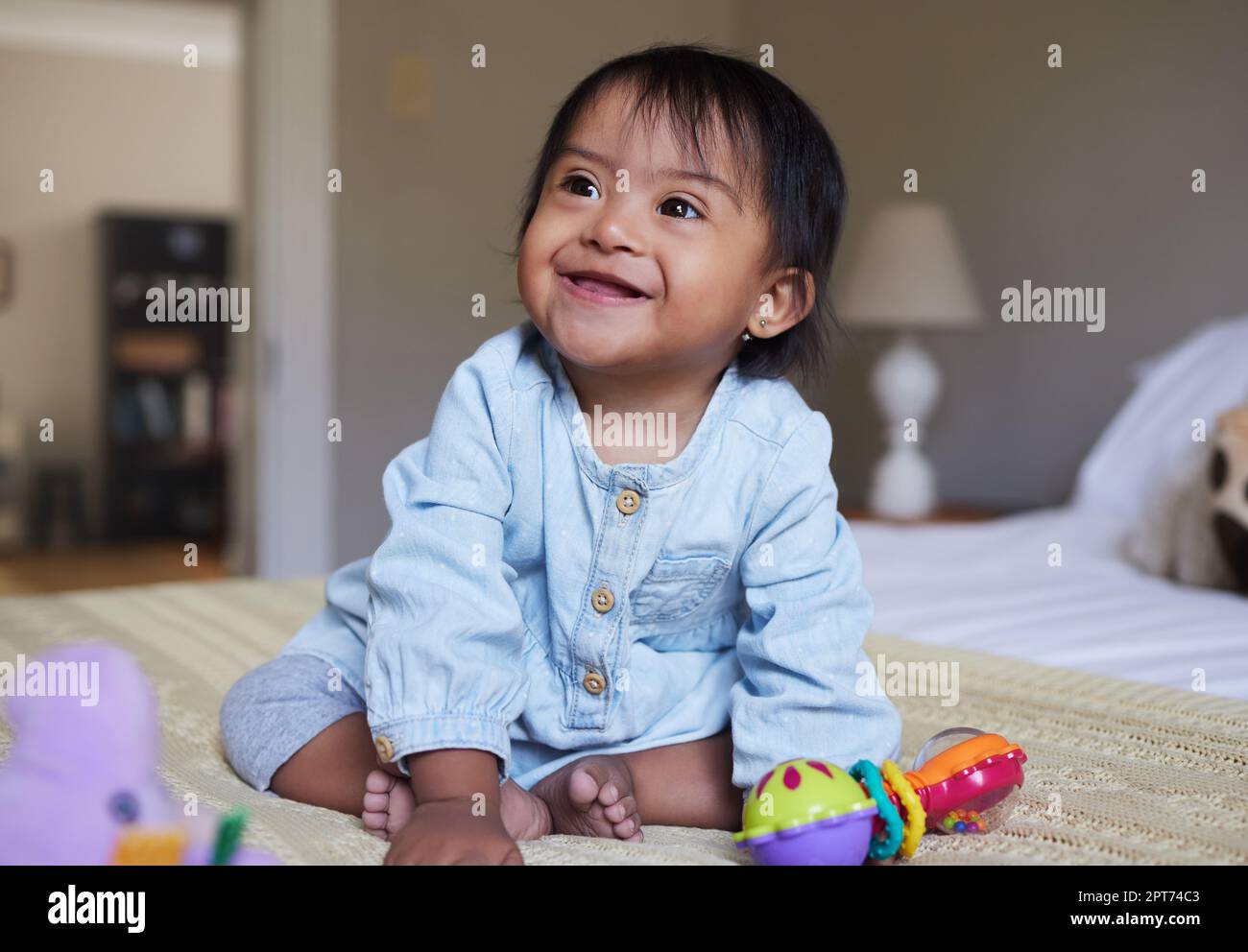 Down Syndrome, smile and happy baby relax on bed having fun, play with toys and enjoy happiness at home. Intellectual disability, mentally disabled an Stock Photo