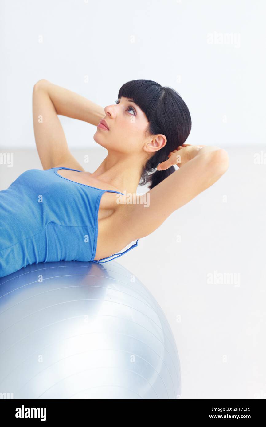 Working towards a toned midriff. Healthy young woman doing sit-ups on an exercise ball Stock Photo