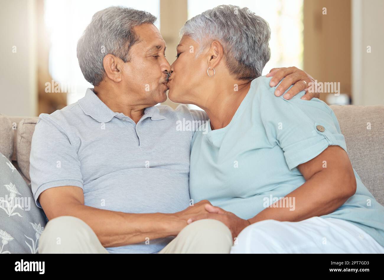 Senior couple, kiss and love at home while sitting on sofa in lounge to bond, relax and enjoy free time during retirement. Old man and woman sharing r Stock Photo