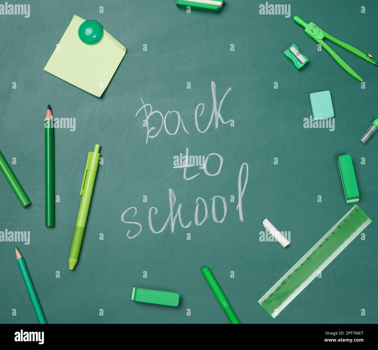 School supplies on empty green chalk board, top view. Chalk lettering back to school Stock Photo