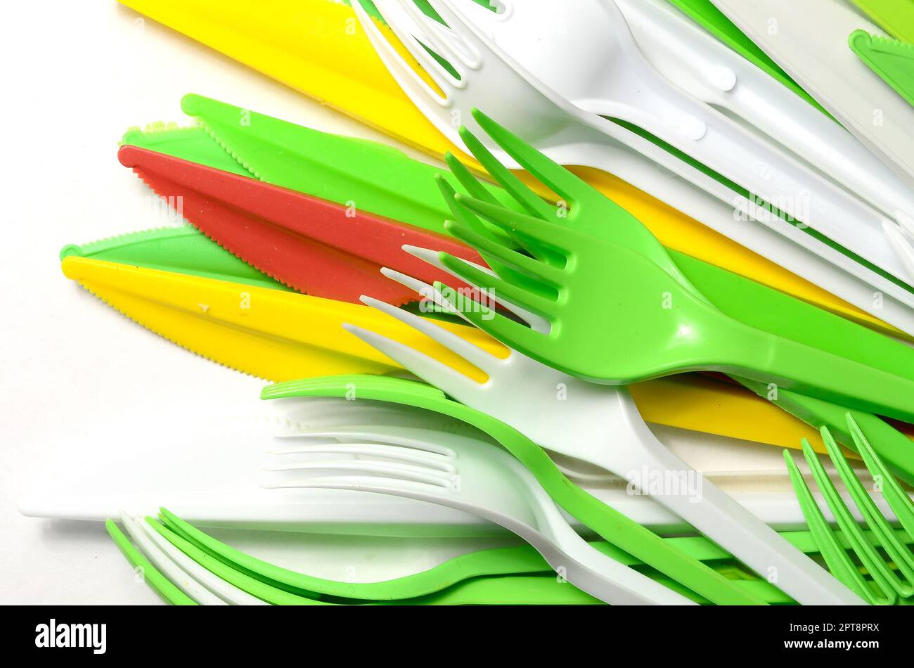 Pile of bright yellow, green and white plastic kitchenware single use appliances on white