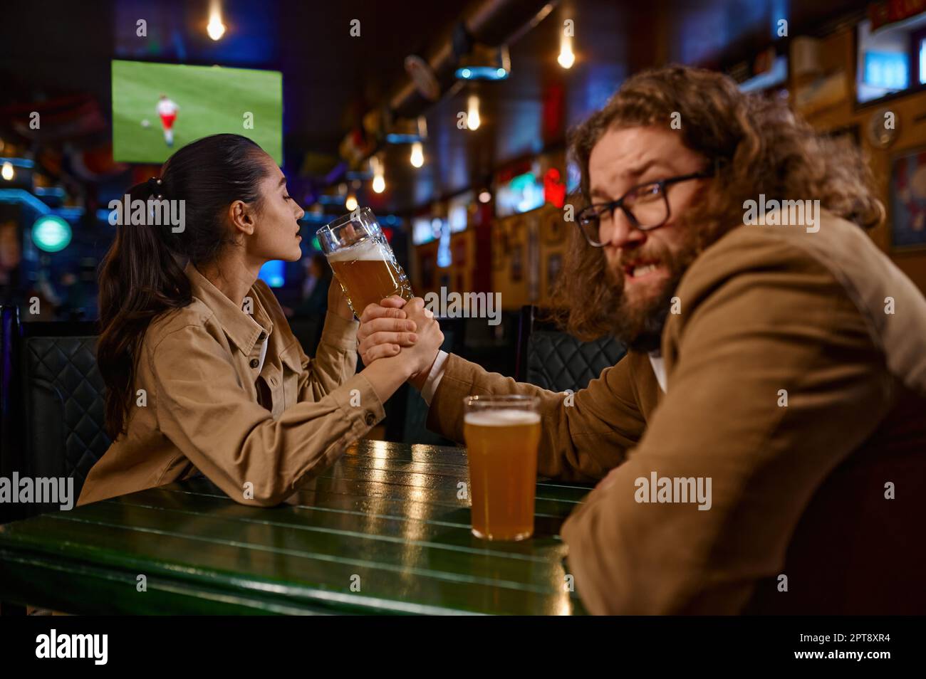Arm wrestling challenge between man and woman at pub. Happy friends