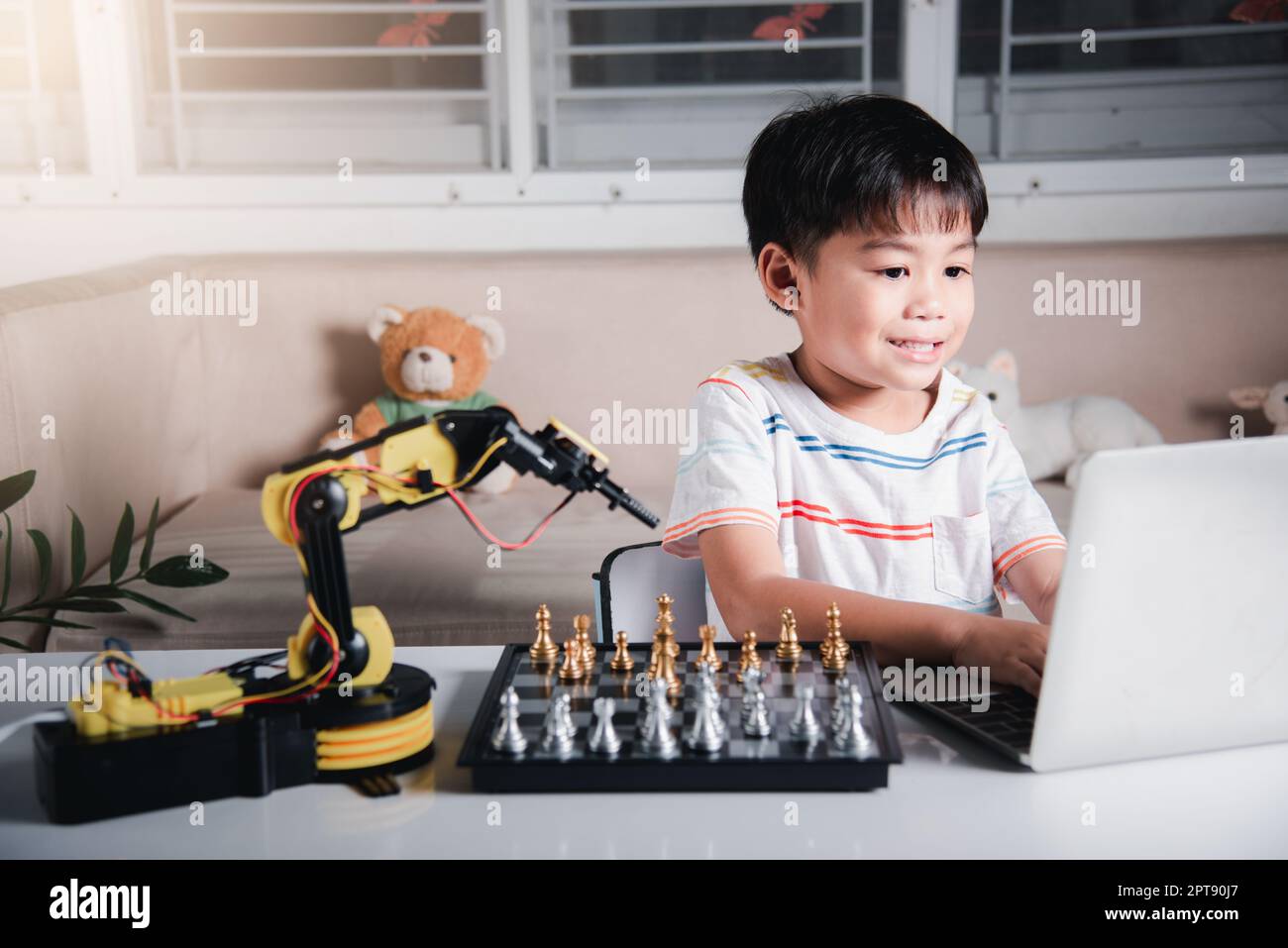 Asian little boy programming code to robot machine arm on laptop for ...