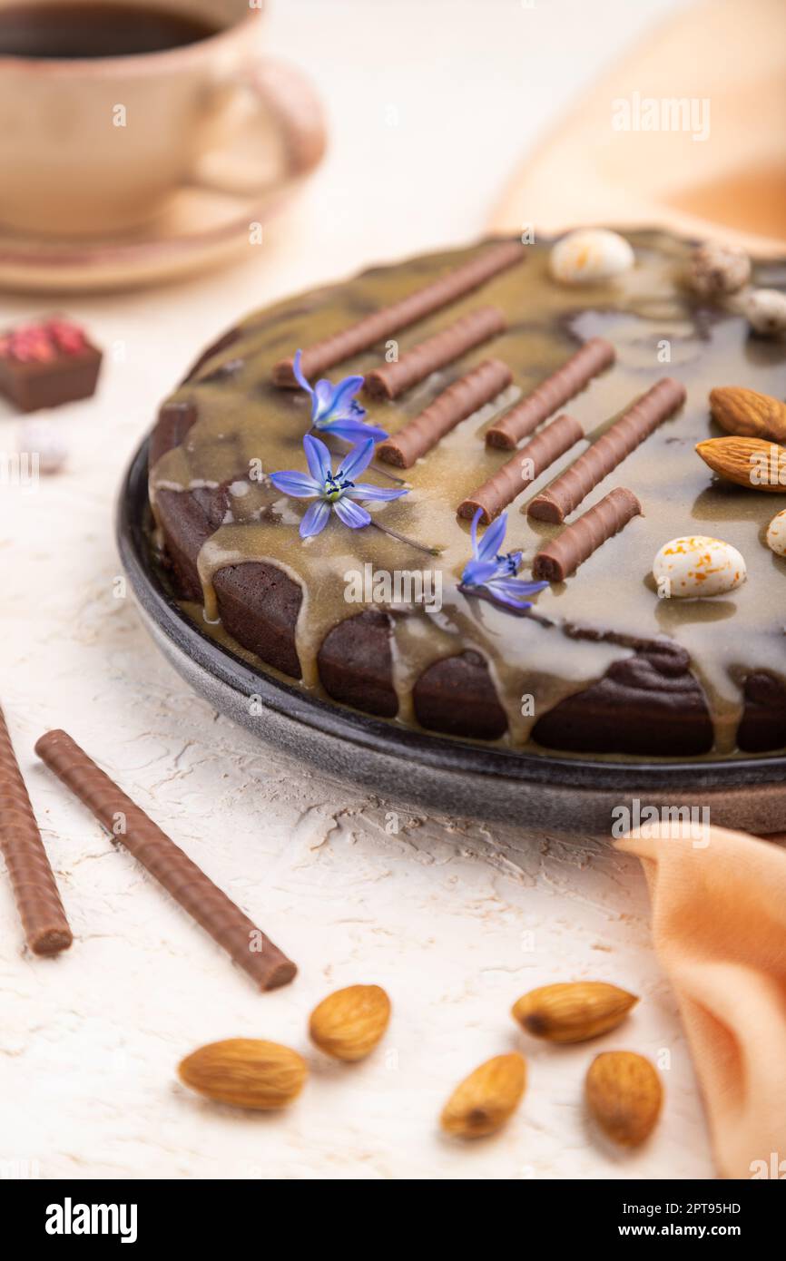 Homemade chocolate brownie cake with caramel cream and almonds with cup of coffee on a white