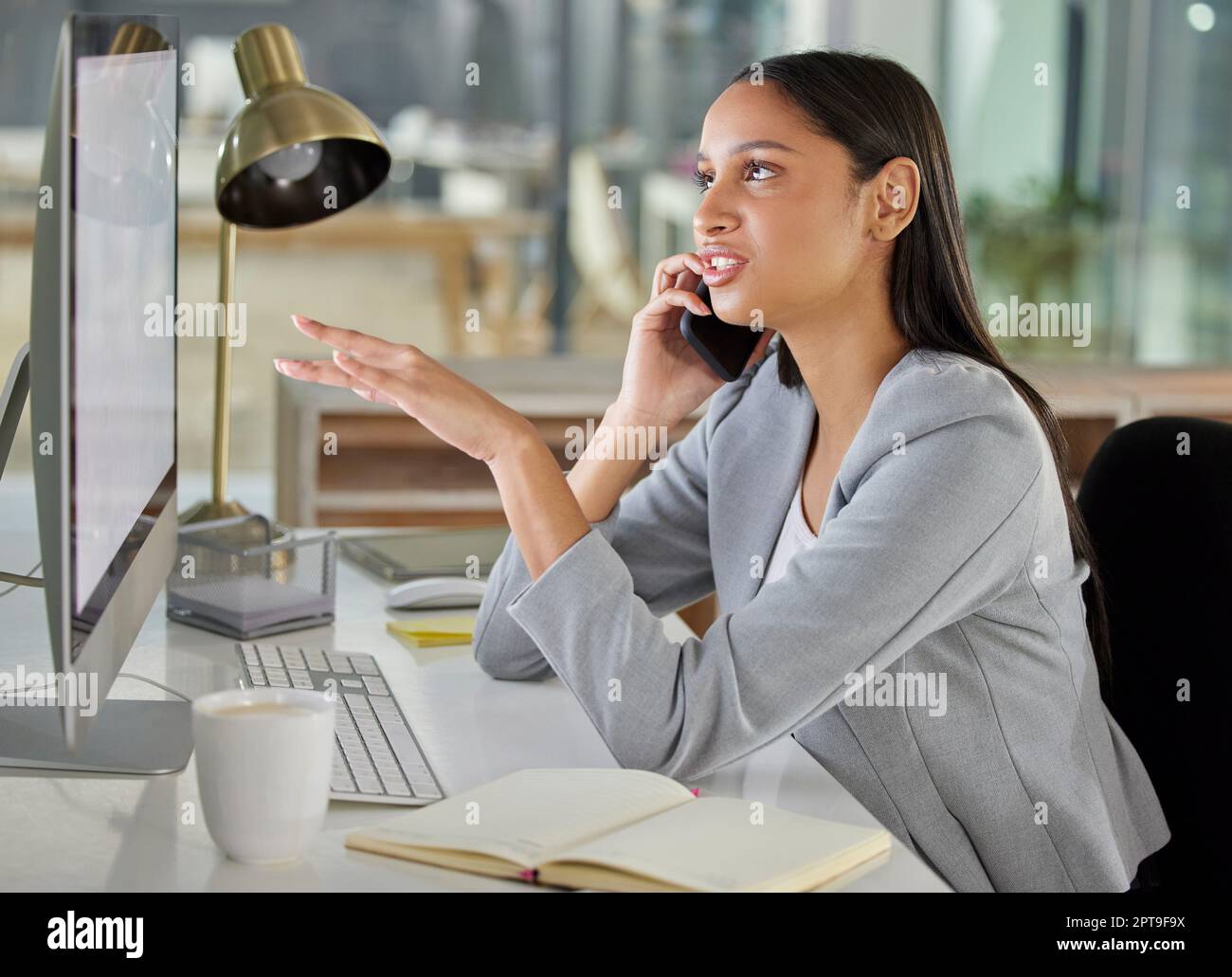 Consistent work keeps the numbers up. a young businesswoman using a smartphone and computer in a modern office Stock Photo