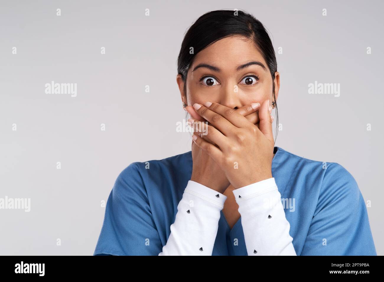 Sleep in makeshift tombs isnt peace, Im here, at least. Portrait of a shocked young doctor covering her mouth in scrubs against a white background Stock Photo