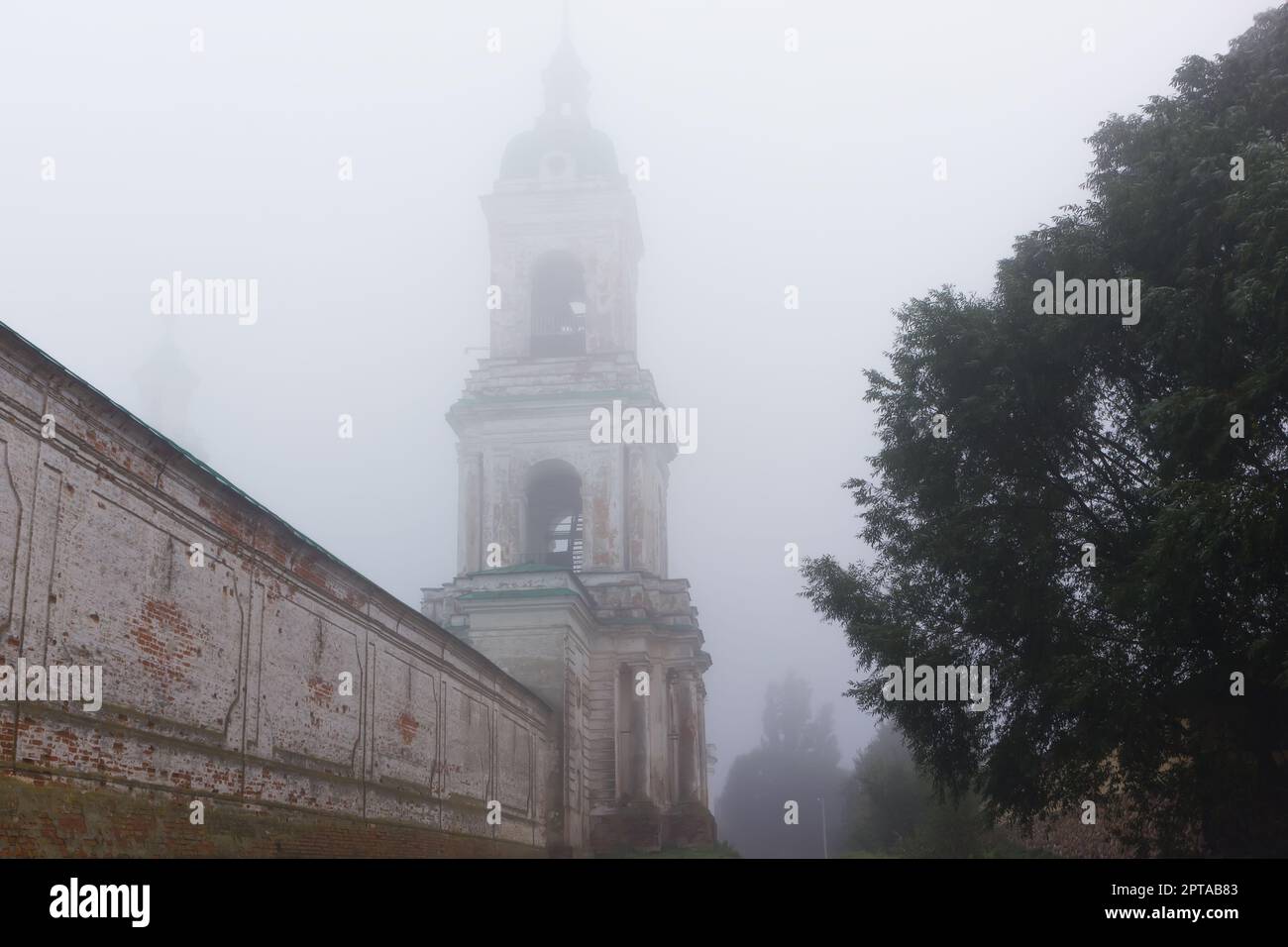 Bell tower and the brick wall of the ancient Spaso-Yakovlevsky Orthodox monastery covered with autumn morning fog. Russian classical architecture of t Stock Photo