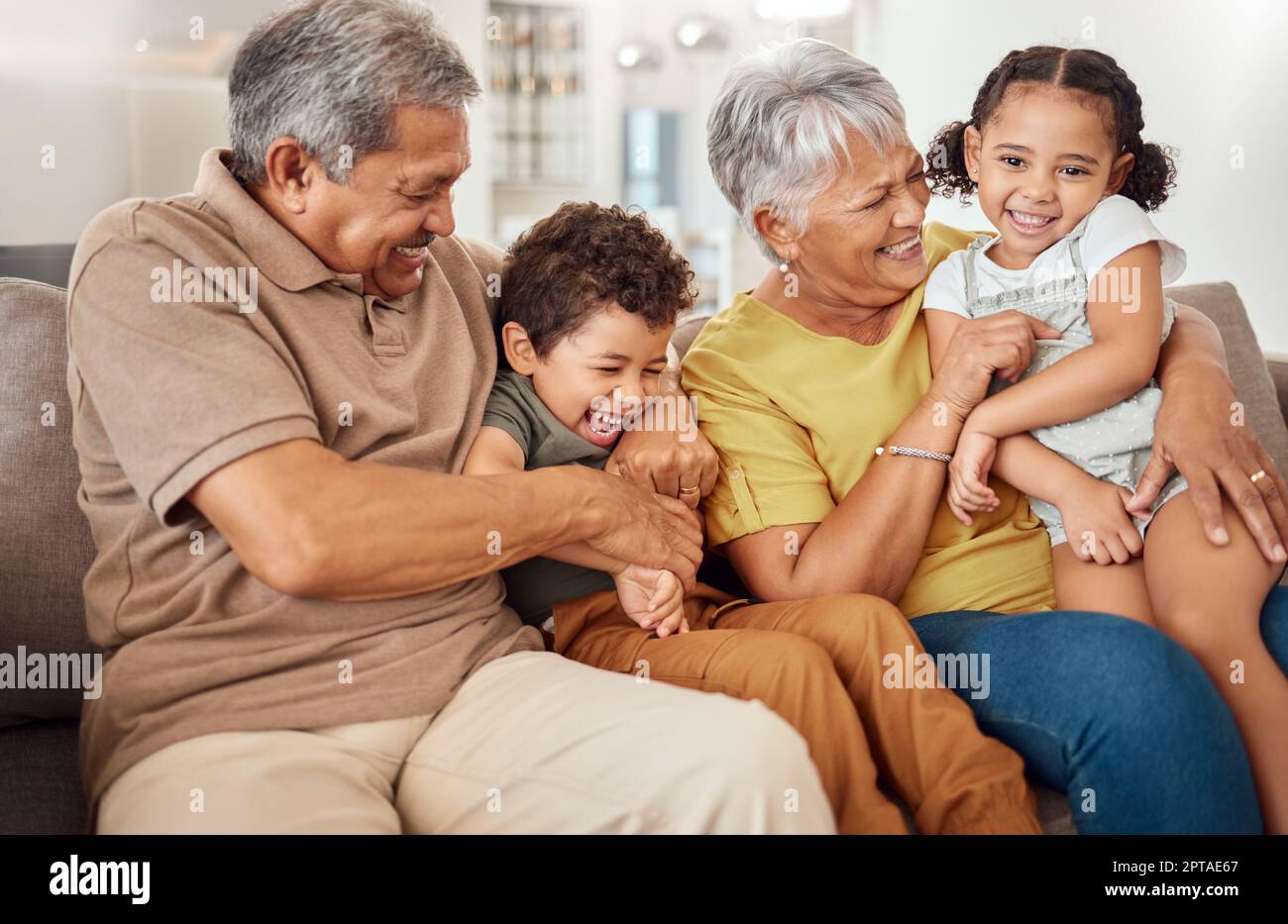 Family, happy and grandparents with children on sofa playing tickle game for bonding fun in home. Love, care and joyful smile together in Mexico famil Stock Photo
