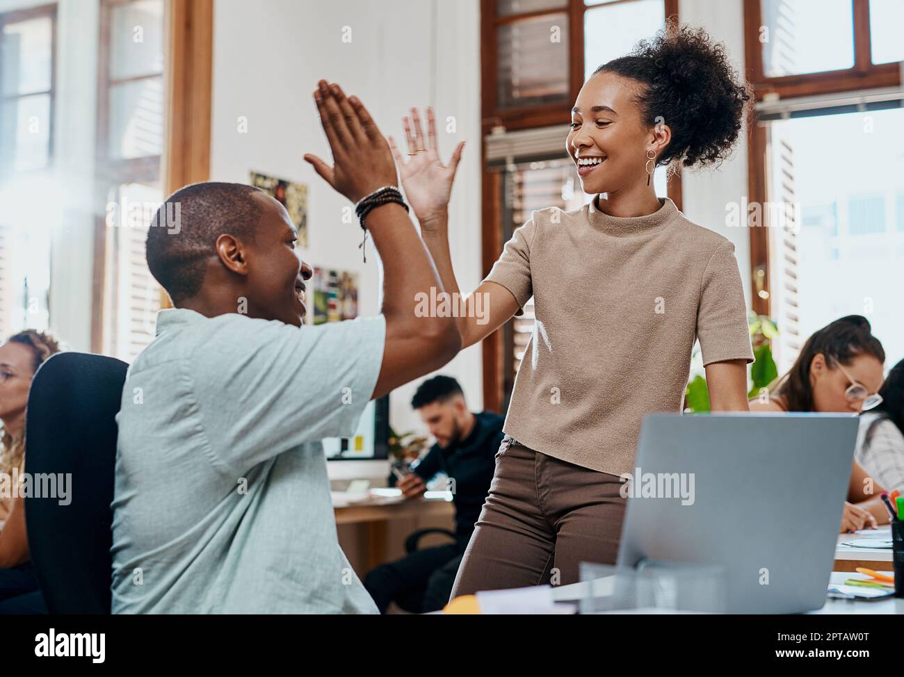 Thats why youre awesome to work with. a young businessman and businesswoman giving each other a high five while using a laptop in an office Stock Photo