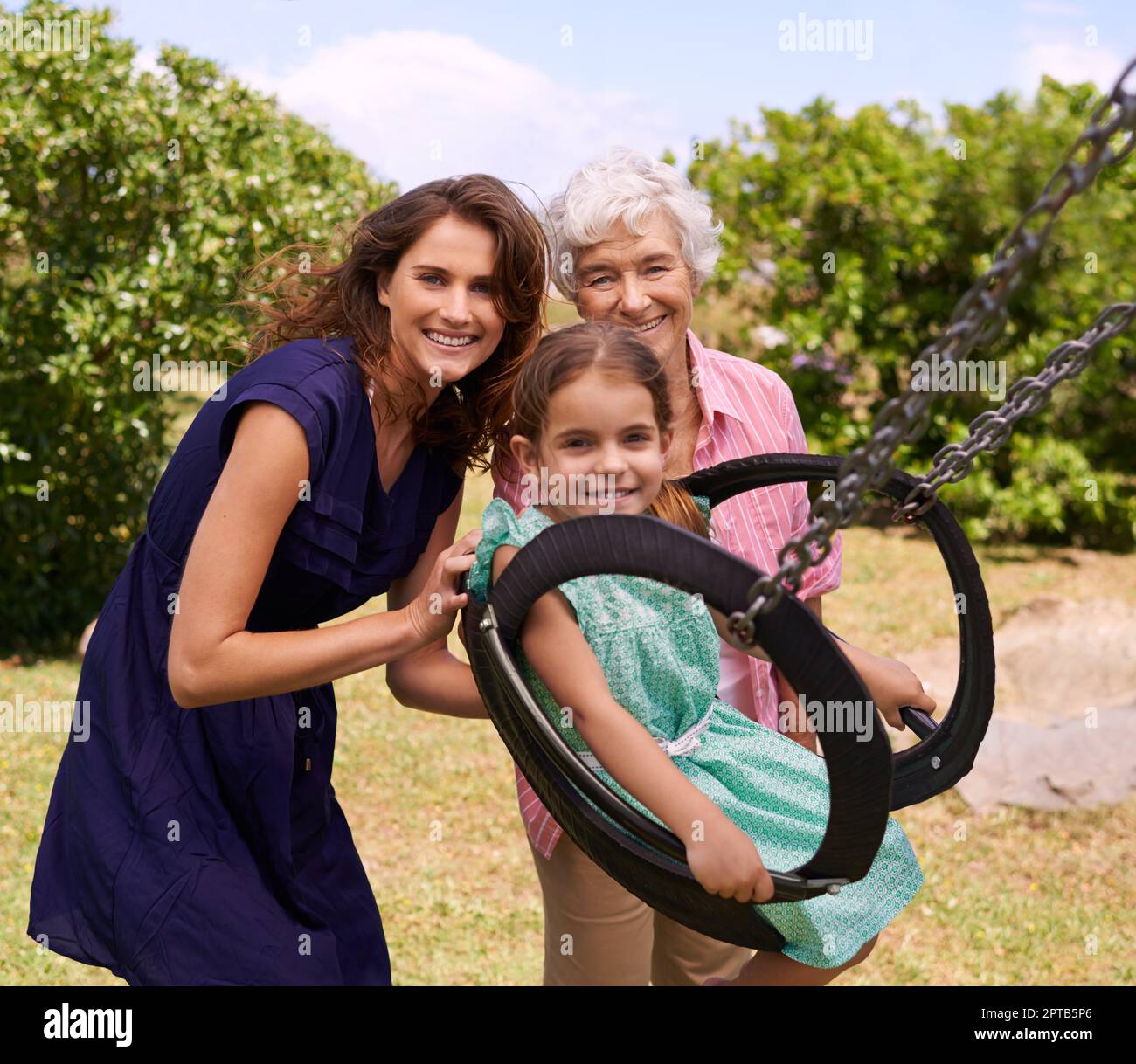 Lets make me go high. a little girl being pushed on a swing outside Stock Photo