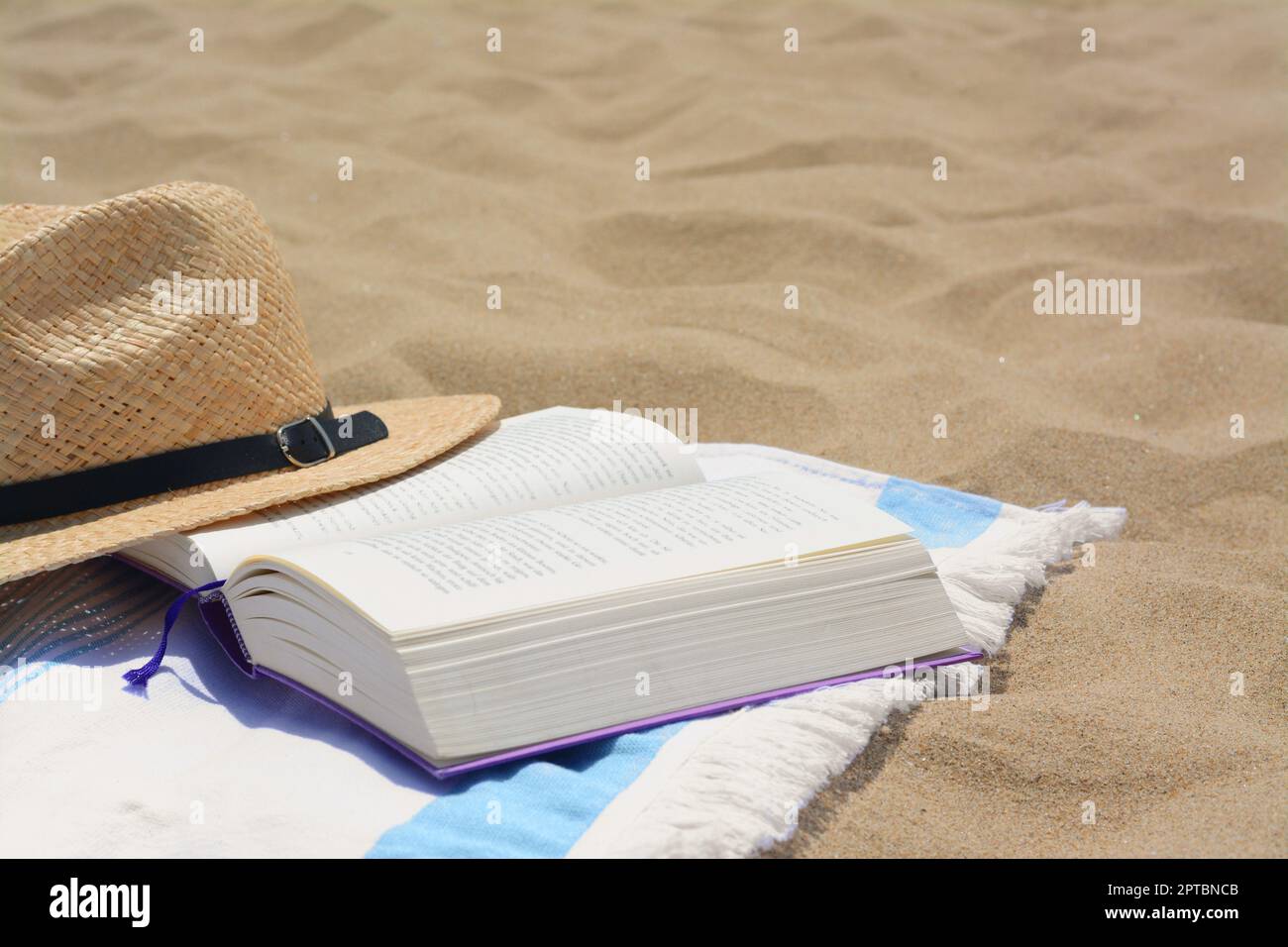 Beach towel with open book and straw hat on sand, space for text Stock ...
