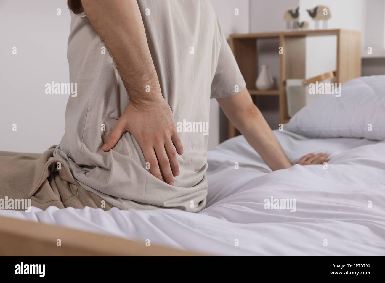 Man suffering from back pain while sitting on bed in room, closeup. Symptom of scoliosis Stock