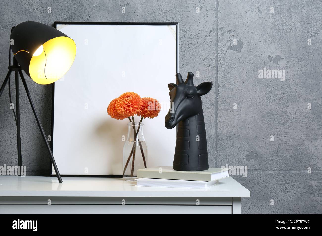 Stylish decor, vase with flowers, picture and desk lamp on white table ...