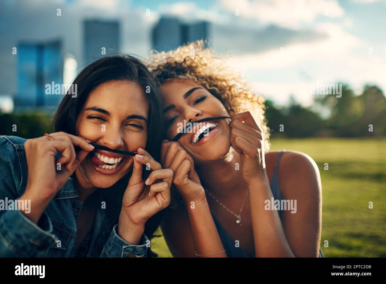 We love being silly together. Cropped portrait of two attractive young girlfriends making a moustache with their hair in a park Stock Photo