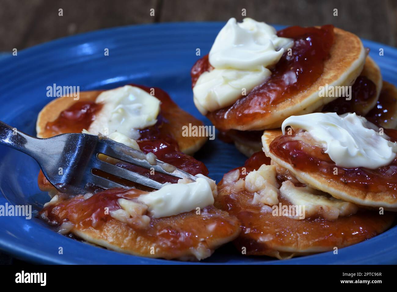 A close-up of a fork cutting into a messy plateful of pikelets/pancakes to illustrate an overindulgent eating frenzy of sweet, fatty desserts Stock Photo