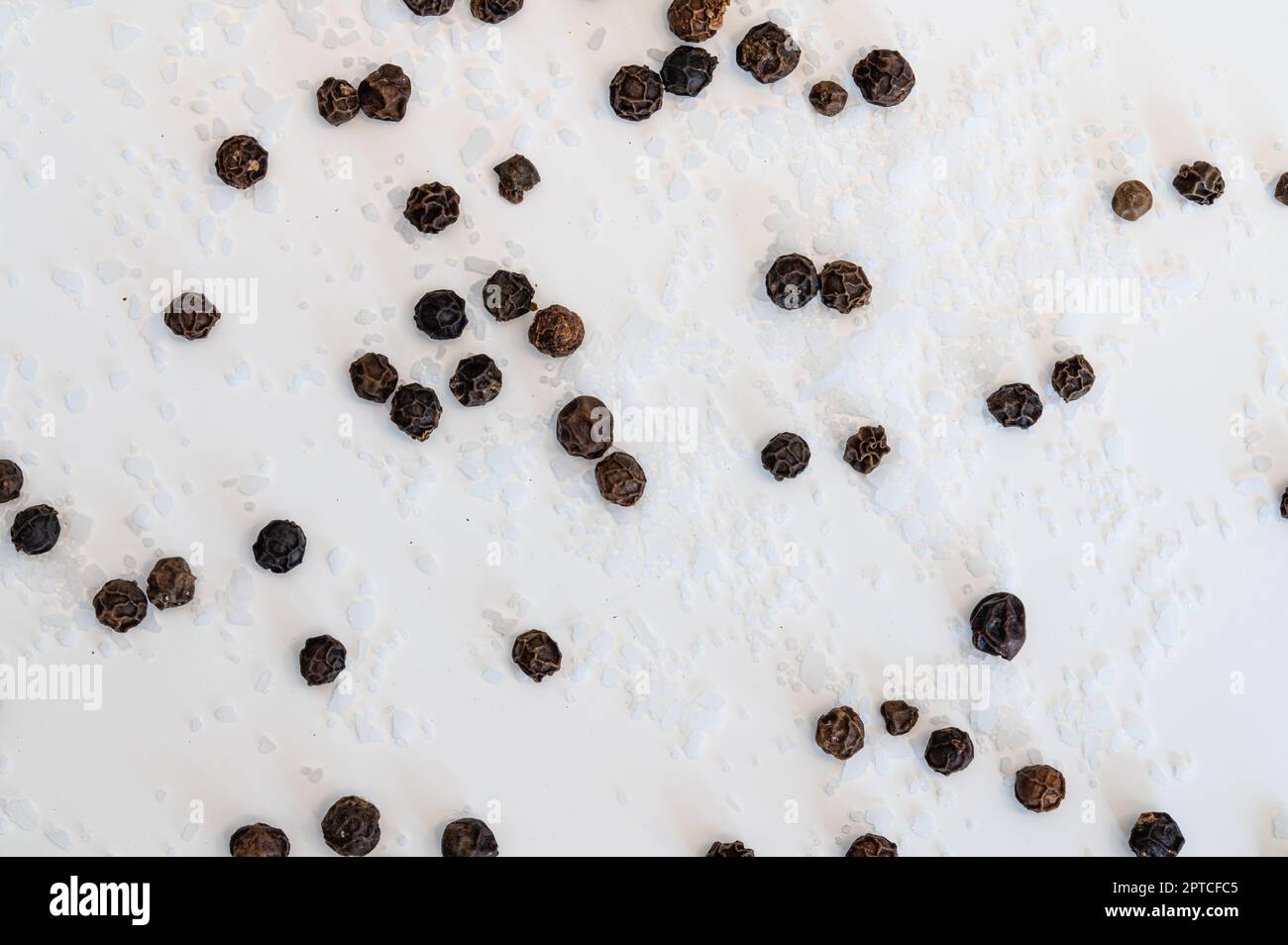 Close up of table salt and black peppercorns scattered on a white background Stock Photo
