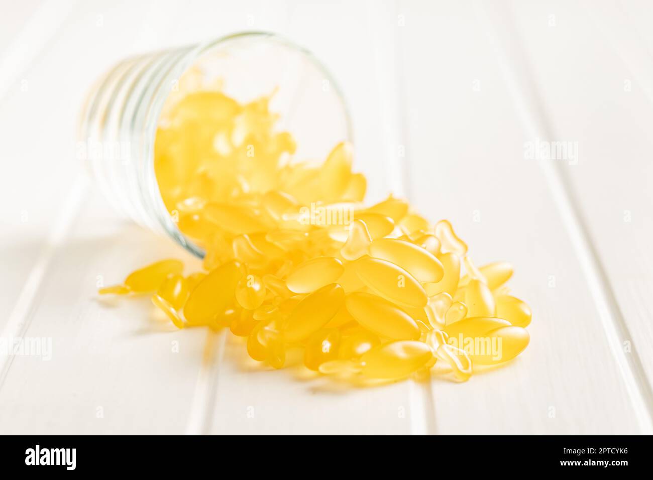 Fish oil capsules. Yellow omega 3 pills in glass on the white table. Stock Photo