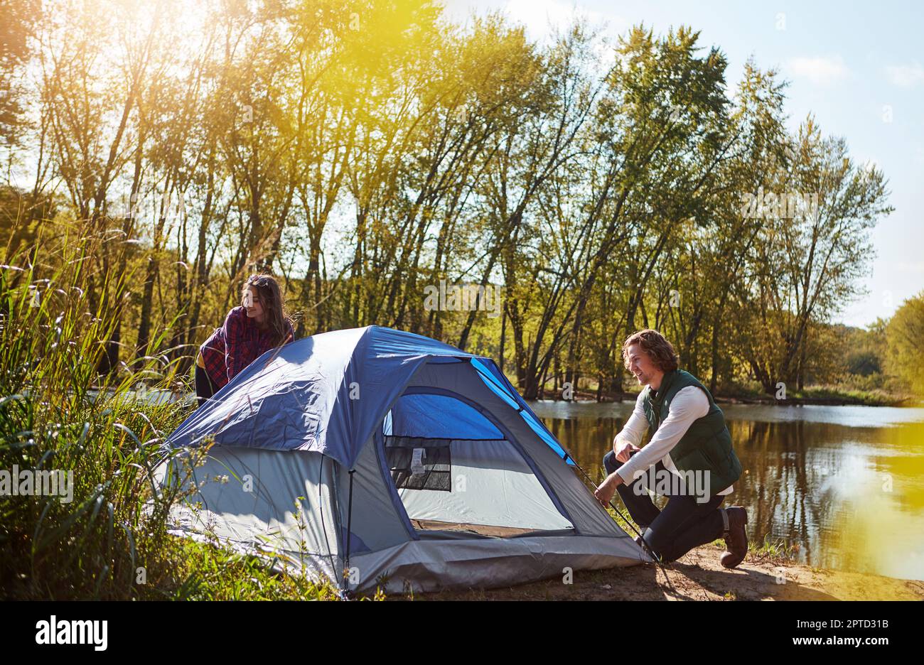 Home is where you pitch your tent. an adventurous setting up their tent by the lake. Stock Photo