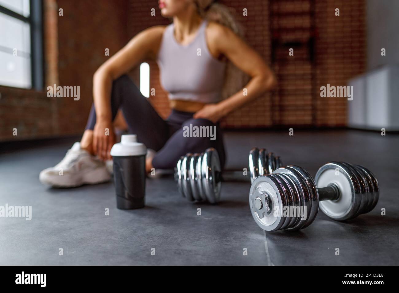 Tired athlete woman taking rest after intense training sitting on floor at gym sportclub Stock Photo