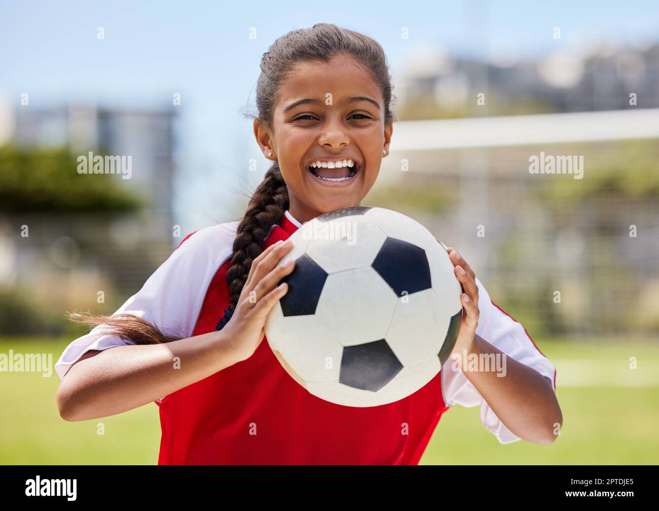 Soccer, sports and happy Indian girl athlete holding a sport ball on a school field. Portrait of fitness, football and exercise of a child smile excit Stock Photo